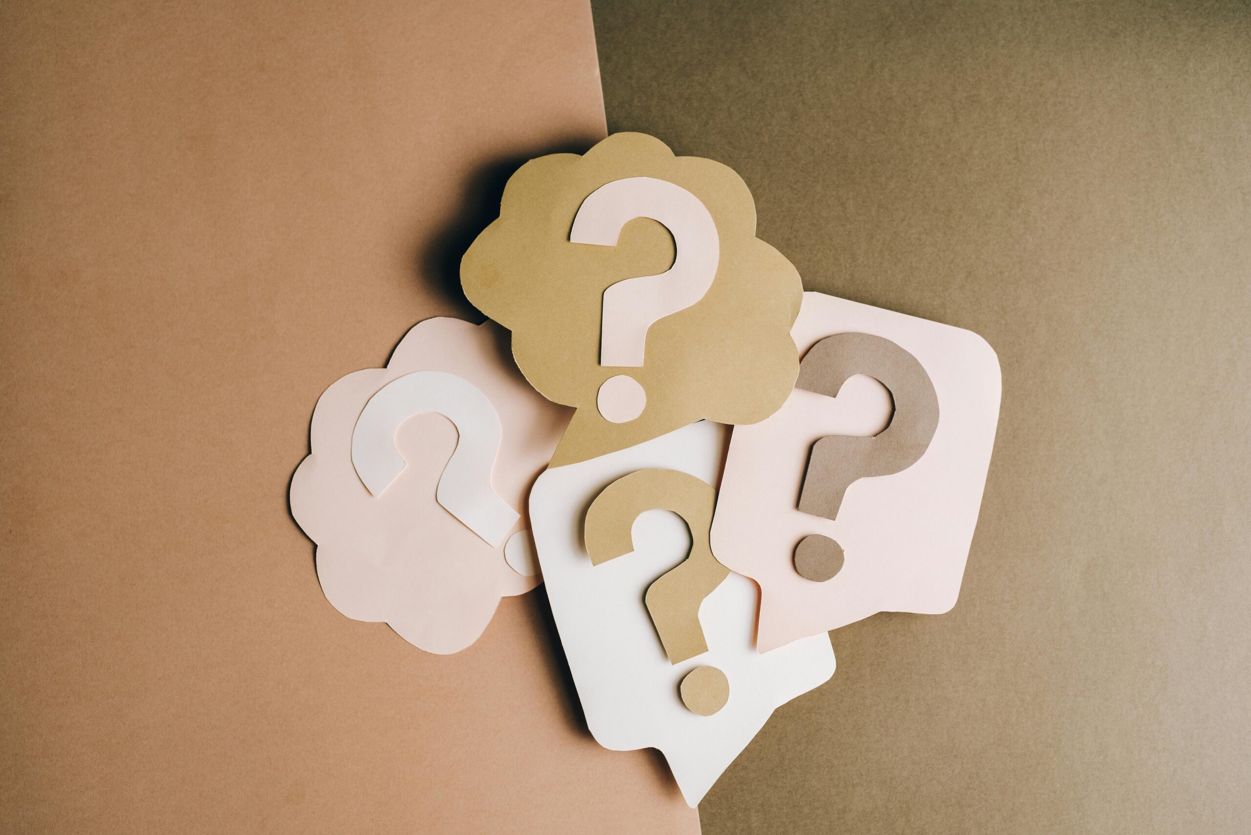 Question mark cutouts in layered paper craft style on a brown backdrop, conceptual art.